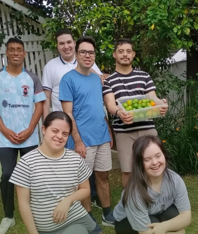 Grupo de adultos atendidos pela Fundação posando juntos no jardim com uma caixa de limões